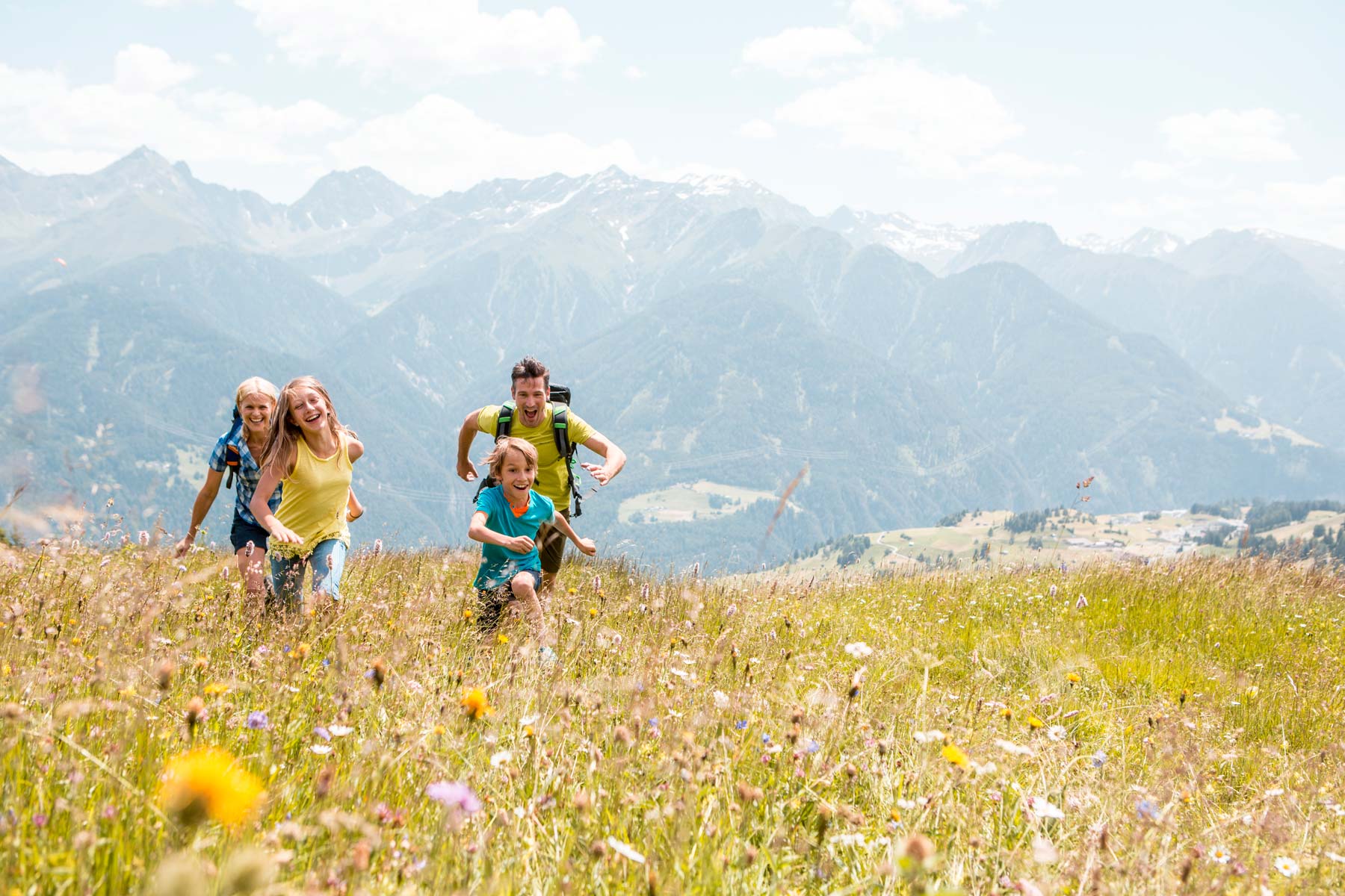 Eine Familie rennt lachend durch ein Feld voller Blumen und Gräser.